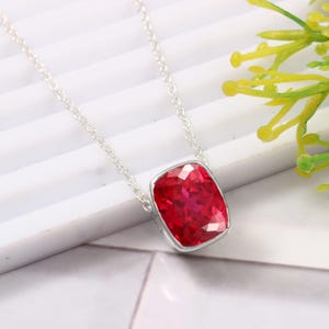 May include: A silver chain necklace with a red gemstone pendant. The gemstone is a cushion cut and has a faceted design.