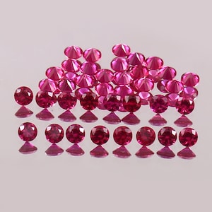 May include: A group of 25 loose round red gemstones, likely rubies, arranged in a pyramid shape on a white surface.