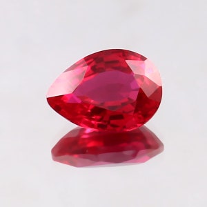 Pode incluir: Uma gema vermelha vibrante em forma de pêra com um corte facetado. A gema está colocada sobre um fundo branco e reflete a luz.