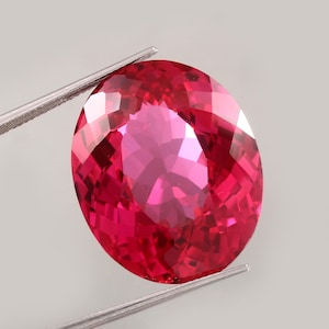 Op de afbeelding: Een levendige roze ovaalvormige edelsteen met een facetgeslepen vorm. De edelsteen wordt vastgehouden door een pincet.