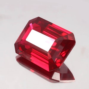 May include: A deep red emerald cut gemstone with a high polish.