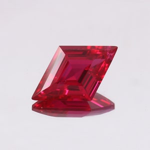 May include: A vibrant red ruby gemstone with a rectangular cut and a slightly elongated shape. The gemstone is faceted and has a high level of brilliance.
