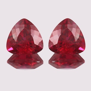 May include: Two red triangular gemstones with a faceted cut. The gemstones are set on a white background.