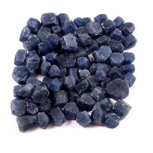 May include: A large pile of rough, faceted, dark blue sapphire gemstones. The stones are various sizes and shapes.