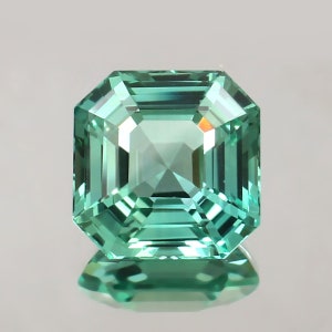 Könnte beinhalten: Ein grüner Smaragdschliff-Edelstein in quadratischer Form.