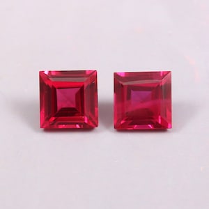 May include: Two square-shaped, red gemstones with a faceted cut.