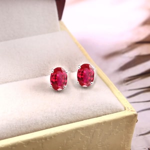 Puede incluir: Un par de pendientes de plata con piedras preciosas rojas de forma ovalada.