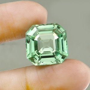 Könnte beinhalten: Ein hellgrüner Smaragdschliff-Edelstein mit quadratischer Form.