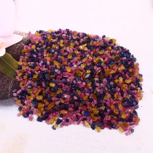 Pode incluir: Um monte de pequenas pedras preciosas ásperas e coloridas. As pedras preciosas são uma mistura de rosa, azul e amarelo.