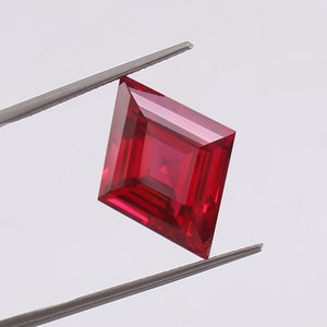 May include: A deep red square-shaped gemstone with a faceted cut, held by tweezers against a white background.