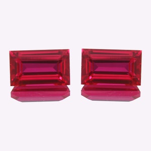 Peut inclure: Deux pierres précieuses rectangulaires rouge vif avec une taille facetée. Les pierres précieuses sont posées sur un fond blanc.
