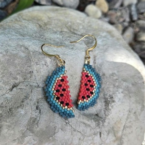 May include: Beaded earrings in a watermelon slice design. The earrings are made with red, black, and blue beads, and have gold-coloured ear wires. A fun and colourful accessory.