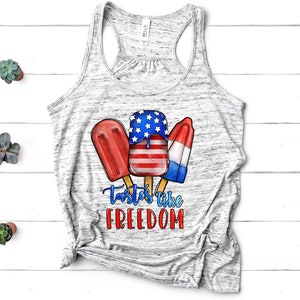 May include: A gray tank top with a graphic of three popsicles. The popsicles are red, white, and blue and have a patriotic theme. The text "Tastes like FREEDOM" is printed below the popsicles.