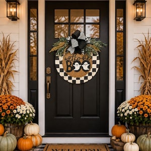May include: A round door sign featuring a black and white checkered pattern, a black and white striped bow, green foliage, and the text "welcome BOO" with two white ghost illustrations. The sign is displayed on a black front door with a welcome mat.
