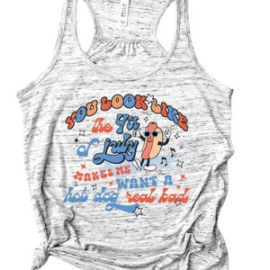 May include: A gray tank top with a white and gray speckled pattern. The text "You look like the 4th of July" is printed in red, orange, and blue. A cartoon hot dog with sunglasses is dancing and the text "Makes me want a hot dog real bad" is printed in red, orange, and blue.