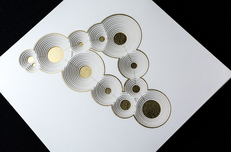 Op de afbeelding: Wit papier met een gouden ontwerp van overlappende cirkels. De cirkels zijn gelaagd om een 3D-effect te cre&euml;ren.
