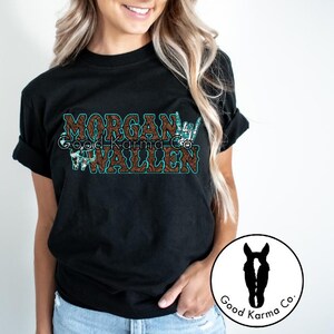 Peut inclure: T-shirt noir avec un motif brun et turquoise qui dit "Morgan Wallen" avec un graphique de geste de la main. Le design est de Good Karma Co.