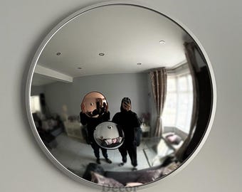 May include: A round, convex mirror with a white frame. The mirror reflects a room with two people holding spherical, reflective objects. The objects are a copper and a silver color. The text "Decor on Décor" is at the bottom.