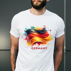 Puede incluir: Camiseta blanca con un dise&ntilde;o de acuarela colorido de la bandera alemana y la palabra "ALEMANIA" impresa debajo.