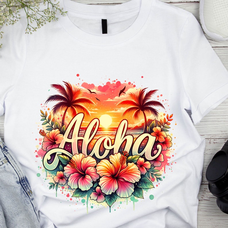 May include: White t-shirt with a colorful graphic design featuring palm trees, a sunset, and the word "Aloha" surrounded by hibiscus flowers.