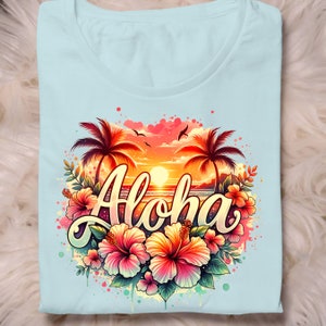 May include: A light blue t-shirt with a colorful graphic design featuring palm trees, a sunset, ocean waves, and the word "Aloha" surrounded by pink hibiscus flowers.