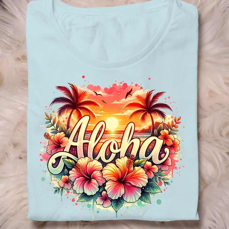 May include: A light blue t-shirt with a colorful graphic design featuring palm trees, a sunset, ocean waves, and the word "Aloha" surrounded by pink hibiscus flowers.