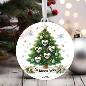 May include: A white, round Christmas ornament featuring a green Christmas tree design with heart-shaped name tags. The names "Mom", "Dad", "Theo", "Chloe", and "Jackie" are displayed. The ornament also includes the text "The Williams family" and the year "2025".