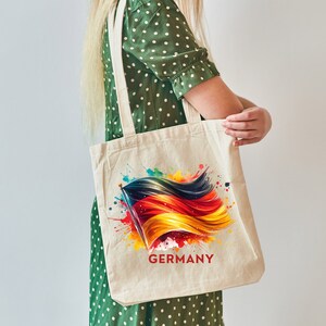 Puede incluir: Una bolsa de lona blanca con un dise&ntilde;o de acuarela colorido de la bandera alemana y la palabra "GERMANY" impresa debajo.
