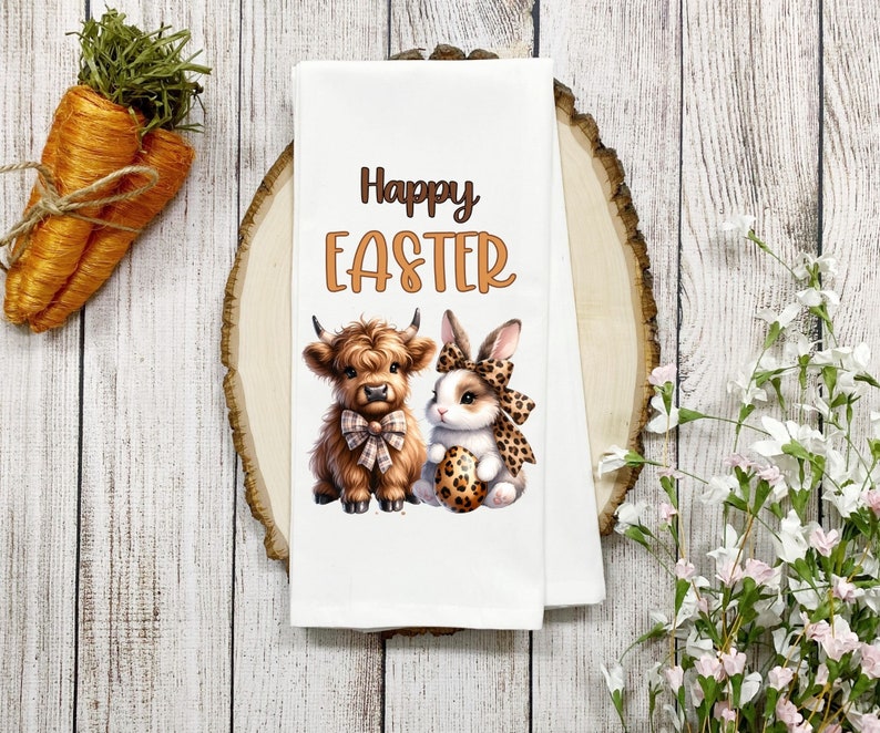 May include: White kitchen towel with a brown Highland cow and a white bunny rabbit holding an Easter egg. The text "Happy Easter" is printed in orange on the towel.