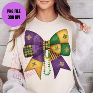 May include: Cream-colored t-shirt featuring a large, colorful bow design. The bow is composed of purple, green, and gold sections with fleur-de-lis symbols and plaid patterns. A strand of beads hangs below the bow. Text on the shirt reads "PNG FILE 300 DPI".