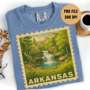 May include: A light blue Comfort Colors t-shirt featuring a vintage-style graphic of a waterfall scene with the text "Glittertini" and "Arkansas" in a postage stamp design. The shirt also has the text "PNG FILE 300 DPI".