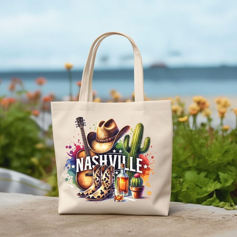 Pu&ograve; includere: Una borsa tote in tela bianca con un design colorato che presenta un cappello da cowboy, una chitarra, stivali, un cactus e una bottiglia di whisky. Il testo "NASHVILLE" &egrave; stampato in lettere nere sulla borsa.
