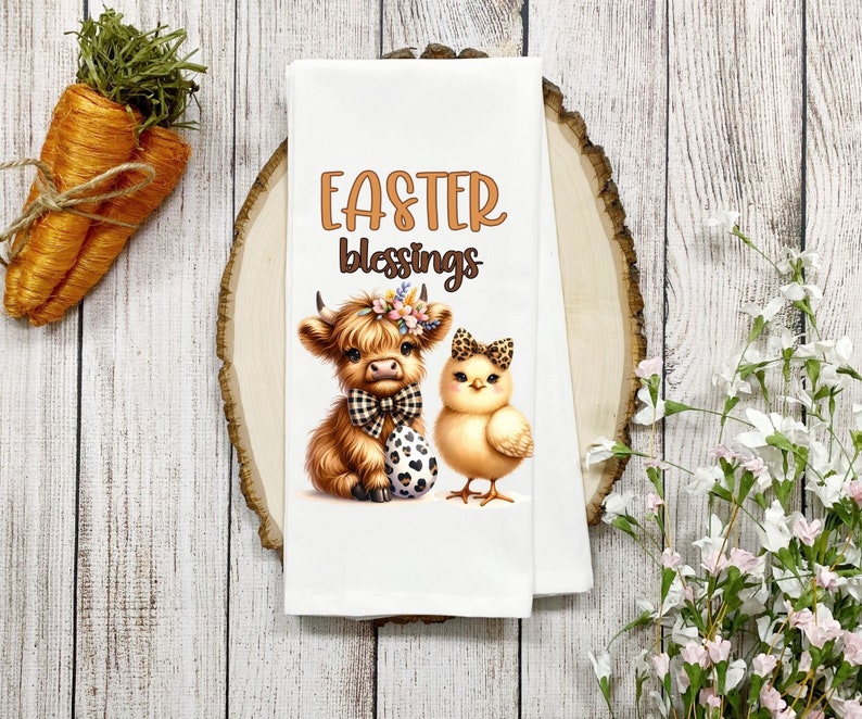 May include: White kitchen towel with a brown Highland cow and a yellow chick. The cow is wearing a black and white bow tie and a floral headband. The chick is wearing a black and white bow. The text "Easter Blessings" is printed in brown above the animals.