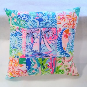 Puede incluir: Una almohada de patchwork con un dise&ntilde;o de velero en el centro. La almohada est&aacute; hecha de una variedad de telas con patrones florales y tropicales en tonos de rosa, azul, verde y blanco.