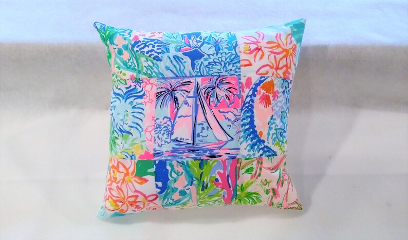 Puede incluir: Una almohada de patchwork con un dise&ntilde;o de velero en el centro. La almohada est&aacute; hecha de una variedad de telas con patrones florales y tropicales en tonos de rosa, azul, verde y blanco.