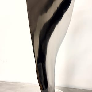 May include: A tall, abstract sculpture with a polished, reflective surface. The sculpture is primarily black and silver, with a curved, blade-like shape. It is mounted on a clear, oval base.