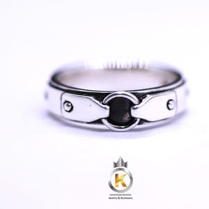 Puede incluir: Un anillo de plata con un diseño circular en el centro y una banda texturizada. El anillo tiene un estilo único y moderno.