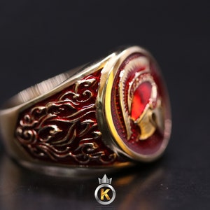 May include: A gold ring with a red and gold enamel design of a Roman helmet. The ring has a detailed design on the band.