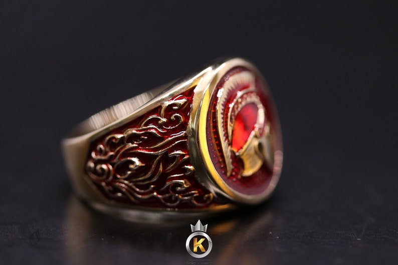 May include: A gold ring with a red and gold enamel design of a Roman helmet. The ring has a detailed design on the band.