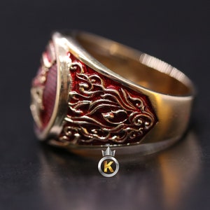 May include: A gold ring with a red enamel design. The ring features intricate details and a raised crest.
