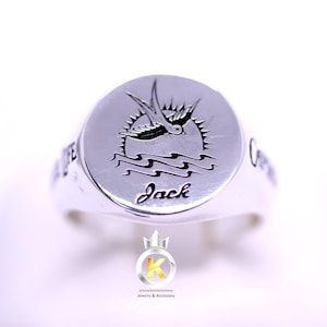 Puede incluir: Anillo de plata con un diseño de golondrina y olas. El anillo está grabado con el nombre "Jack".