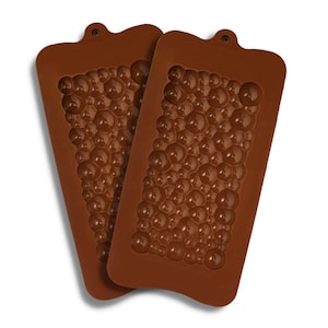 Può includere: Due stampi in silicone marroni per fare il cioccolato. Ogni stampo ha un design di piccole bolle rotonde.
