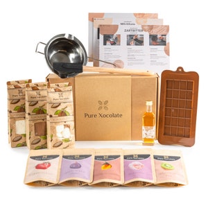 Puede incluir: Un kit para hacer chocolate con una caja marrón, un molde de chocolate, una botella de aceite, un baño maría, una cuchara de madera y seis pequeñas bolsas de sabores de chocolate. La caja tiene el texto "Pure Xocolate" impreso en ella.