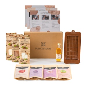 Könnte beinhalten: Ein brauner Karton mit dem Text "Pure Xocolate" auf der Vorderseite. Die Box enthält eine Vielzahl von Zutaten und Zubehör für die Schokoladenherstellung, darunter Kakaopulver, Kakaobutter, Schokoladenformen und eine Flasche Öl. Die Box ist von vier kleinen Beuteln mit Schokoladenaromen umgeben, darunter Mango, Feige, Rose und Kiwi.
