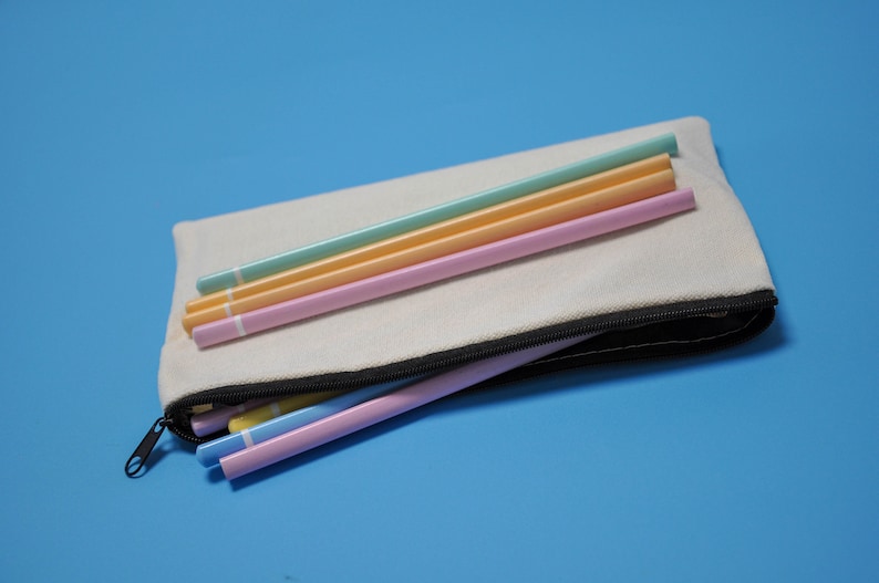 Peut inclure: Une trousse en toile de couleur cr&egrave;me avec une fermeture &eacute;clair noire, ouverte pour r&eacute;v&eacute;ler plusieurs crayons aux couleurs pastel. Les crayons sont dans des tons de bleu, jaune et rose. Le fond est bleu clair uni.