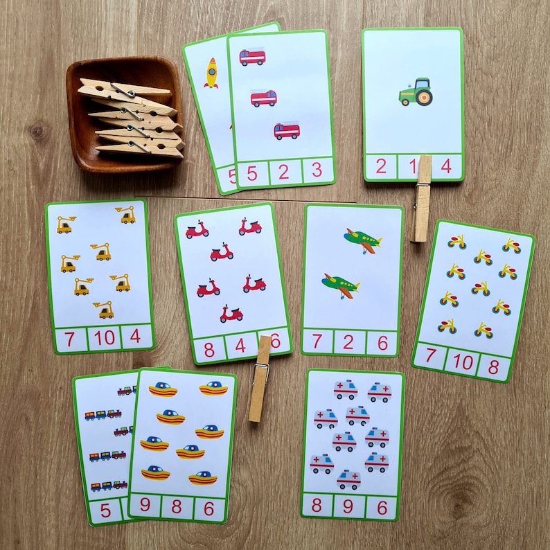 May include: A set of ten printable counting cards featuring various vehicles, including fire trucks, airplanes, tractors, ambulances, and scooters. Each card has a number and a corresponding number of images. The cards are printed on white cardstock with green borders and red numbers.