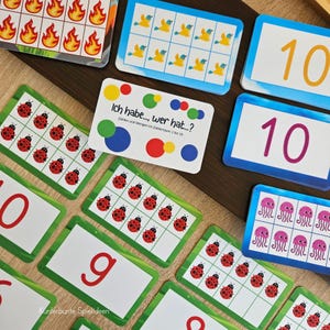 Puede incluir: Una colección de tarjetas de juego educativas con ilustraciones coloridas de mariquitas, llamas, pájaros y medusas, junto a tarjetas con los números 9 y 10. Una tarjeta blanca central presenta el texto Ich habe..., wer hat...?