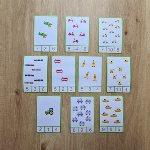 May include: Nine flashcards with colorful illustrations of different vehicles, including airplanes, scooters, tractors, fire trucks, rockets, cranes, ambulances, boats, and trains. Each card has a number and a quantity of the illustrated vehicle.