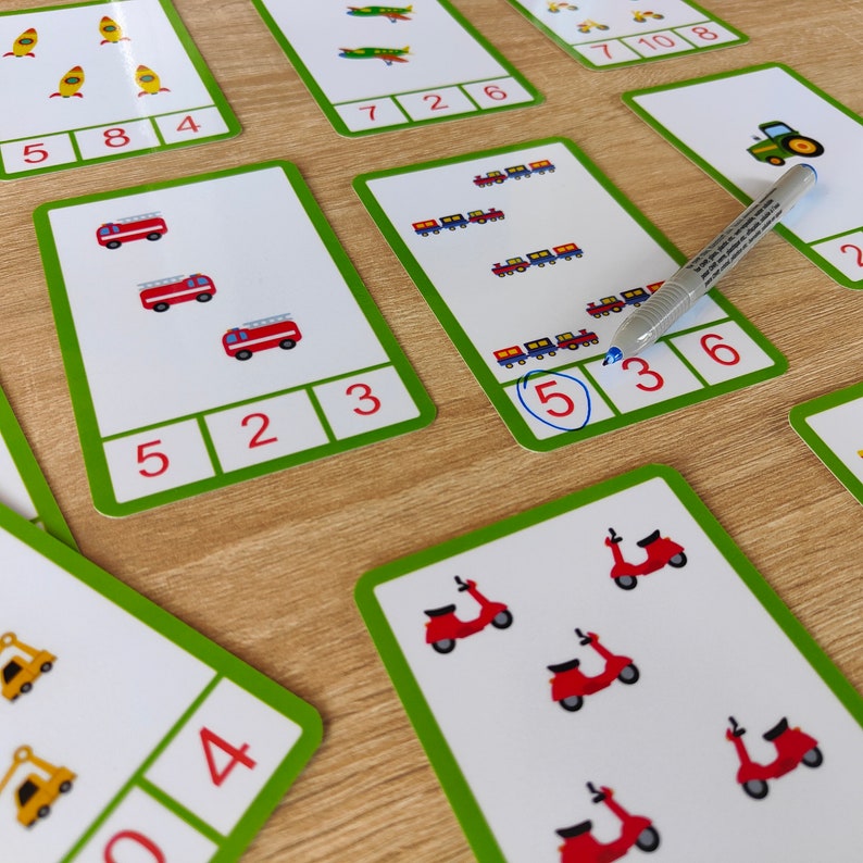 May include: A set of colorful flashcards with images of different objects, such as fire trucks, trains, and scooters. Each card has a number written on it, and the number corresponds to the number of objects on the card. The cards are designed to help children learn to count.