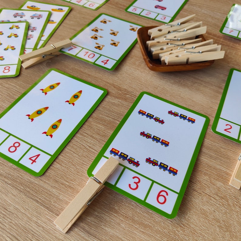 May include: A set of colorful educational flashcards with images of rockets, trains, and cars. The cards have numbers printed on them, and there are wooden clothespins for counting.